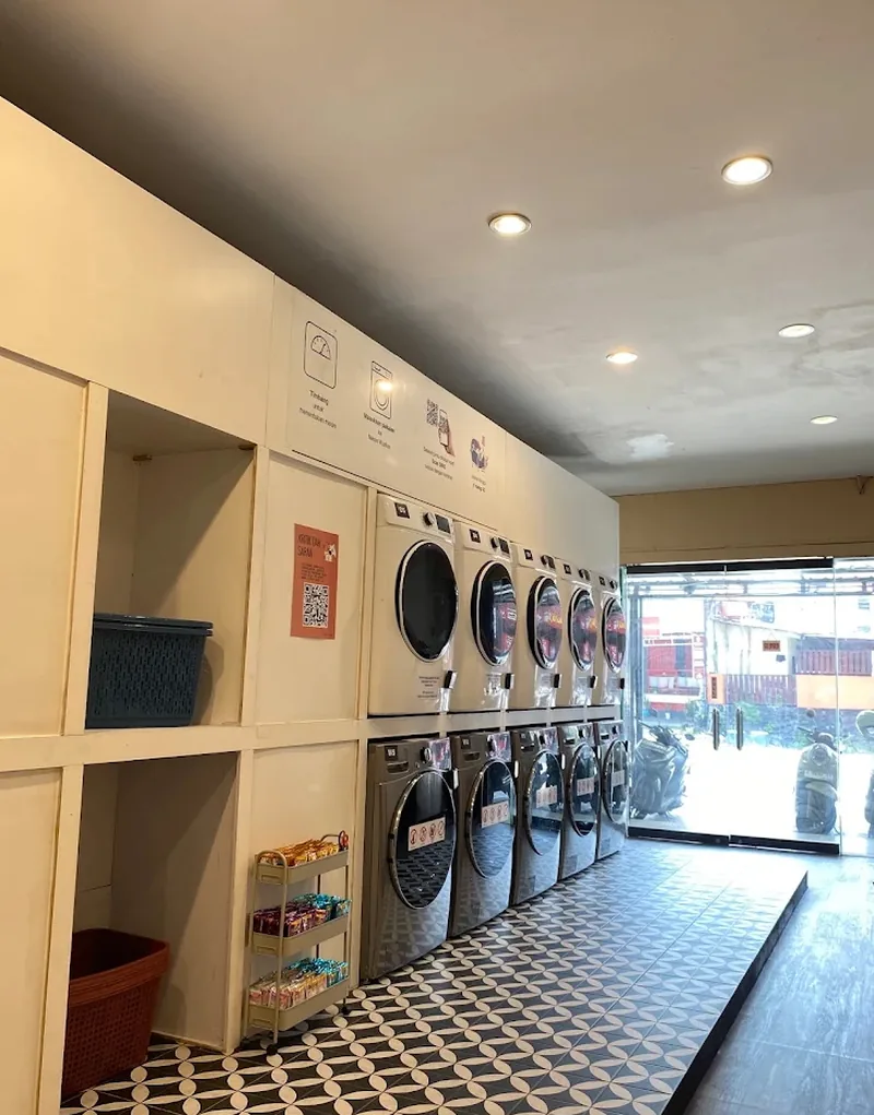 Deretan mesin cuci dan pengering bertumpuk di Temcy Laundry Tembalang, lengkap dengan rak camilan dan keranjang laundry