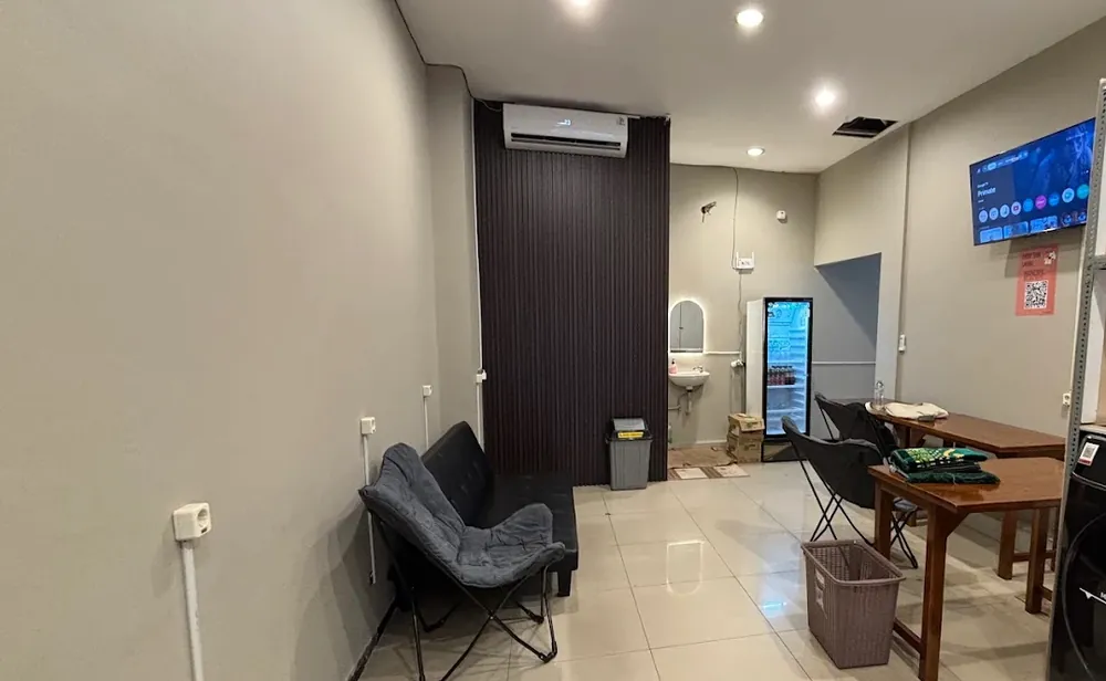 Area tunggu ber-AC di Temcy Laundry Tembalang dengan TV, kursi santai, meja, dan kulkas minuman